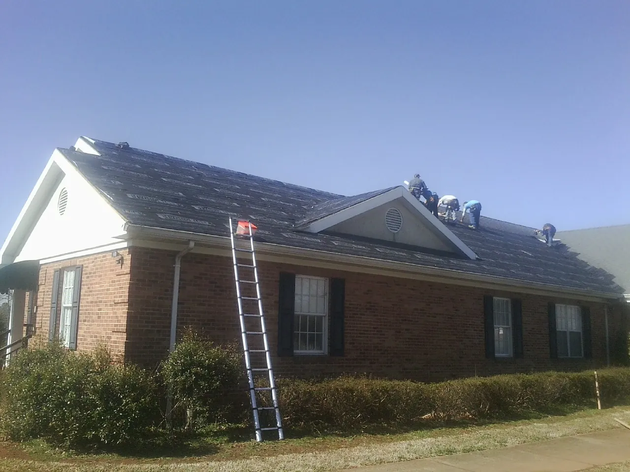 Crew tearing shingles off a brick ranch roof with a ladder set — Emergency Roof Repair work by our crew in Port Matilda