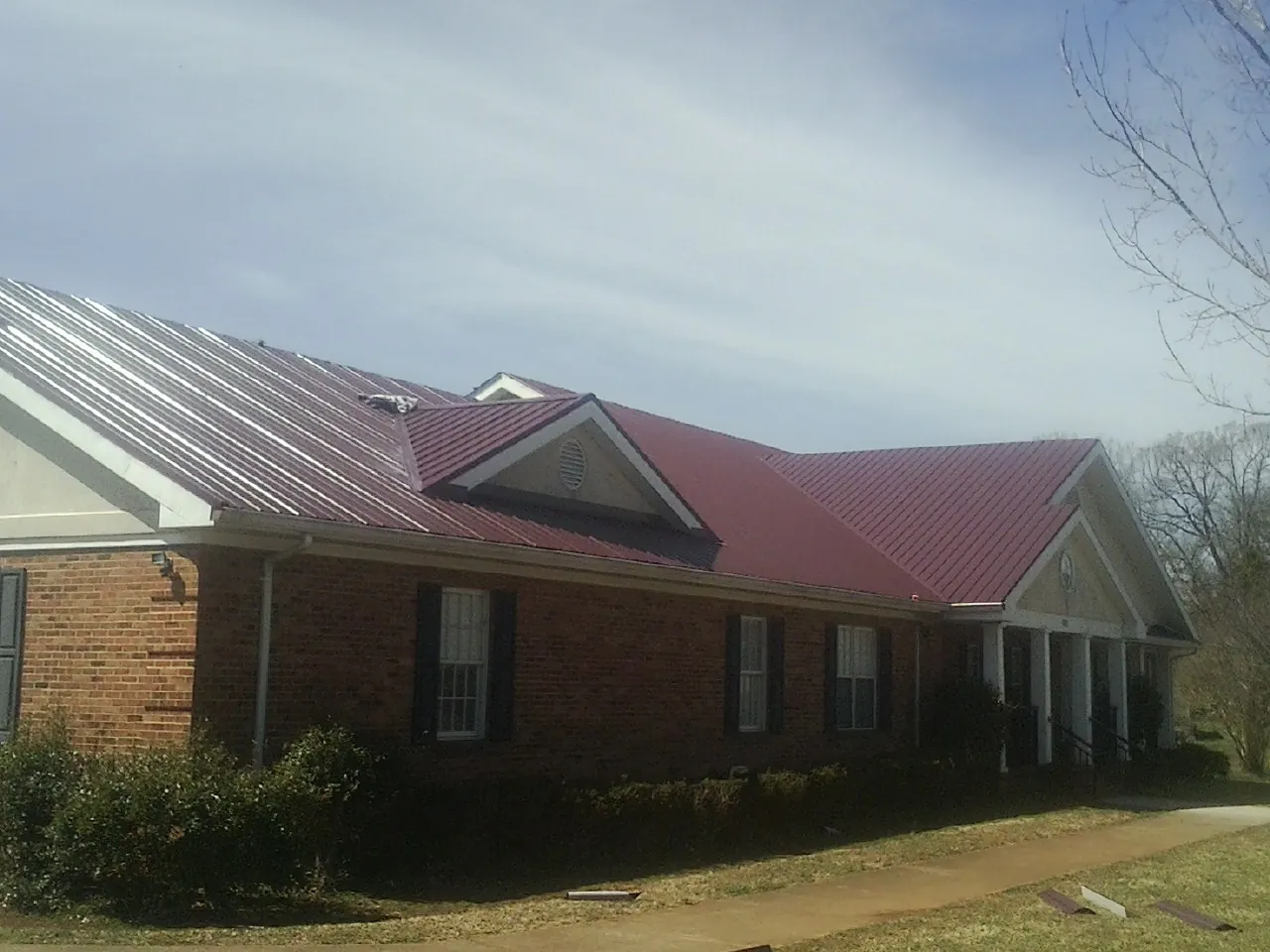Red metal roof with gabled entries on a long brick building, from a Hail Damage Roof Repair job in Port Matilda