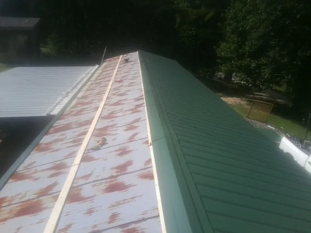 Old rusted panels beside newly installed green metal roofing — Wind Damage Roof Repair by Roofing Brothers in Port Matilda