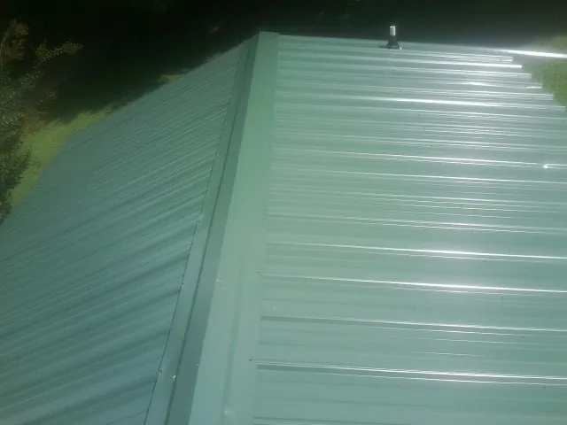 New green metal panels meeting at the ridge of a roof — Flat Roof Repair work by our crew in Port Matilda