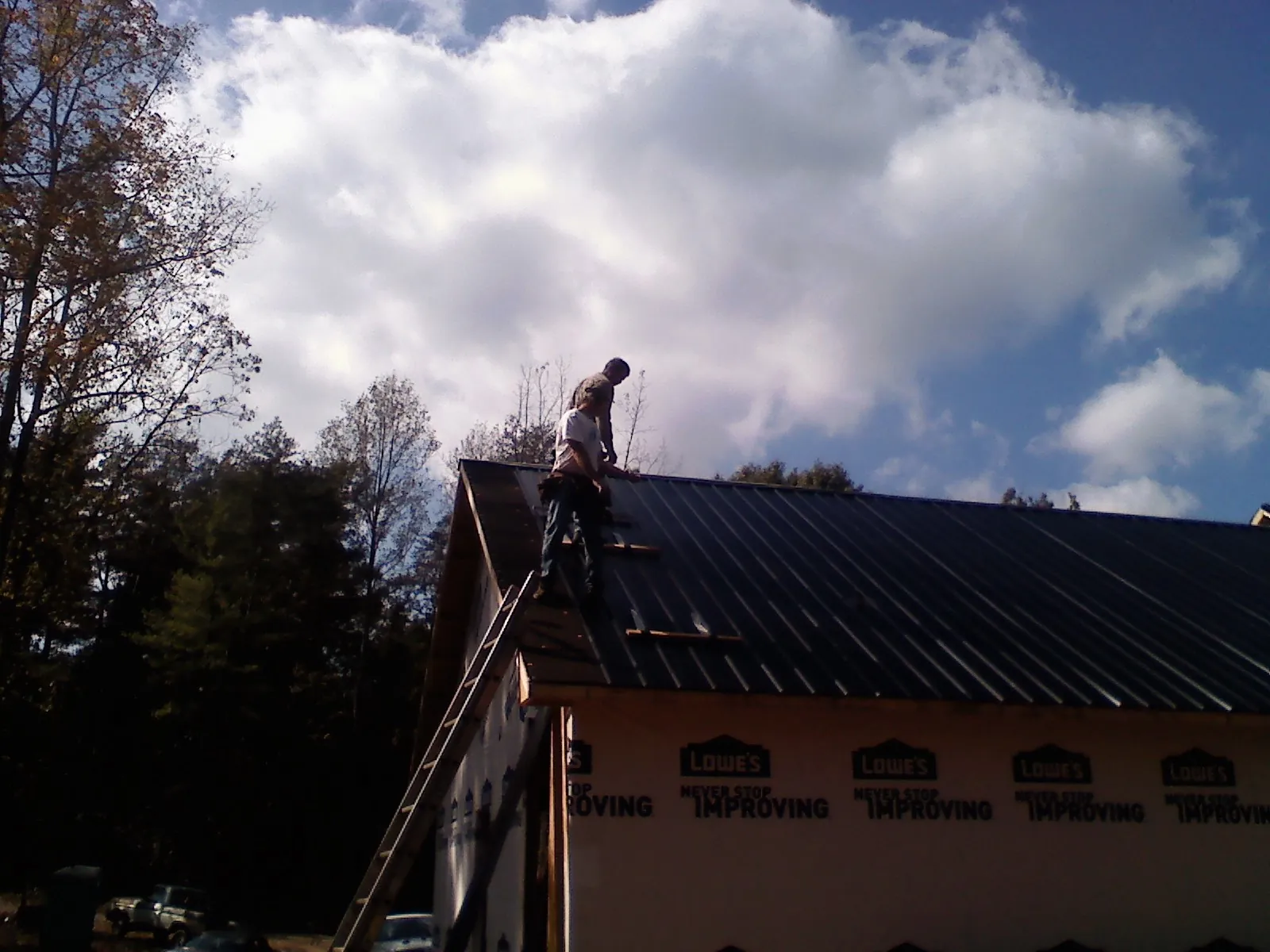 Roofer fastening dark metal panels high against a cloudy sky, from a Roof Inspection job in Port Matilda