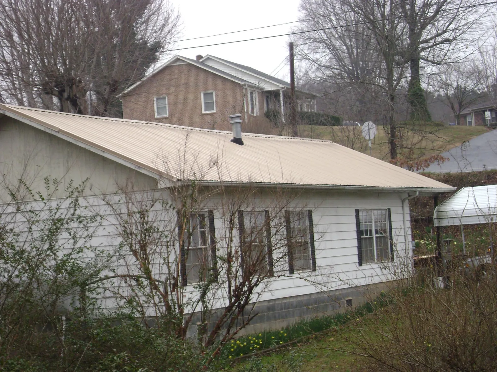 Tan metal roof on a white sided house set into a hillside — Commercial Roofing by Roofing Brothers in Port Matilda