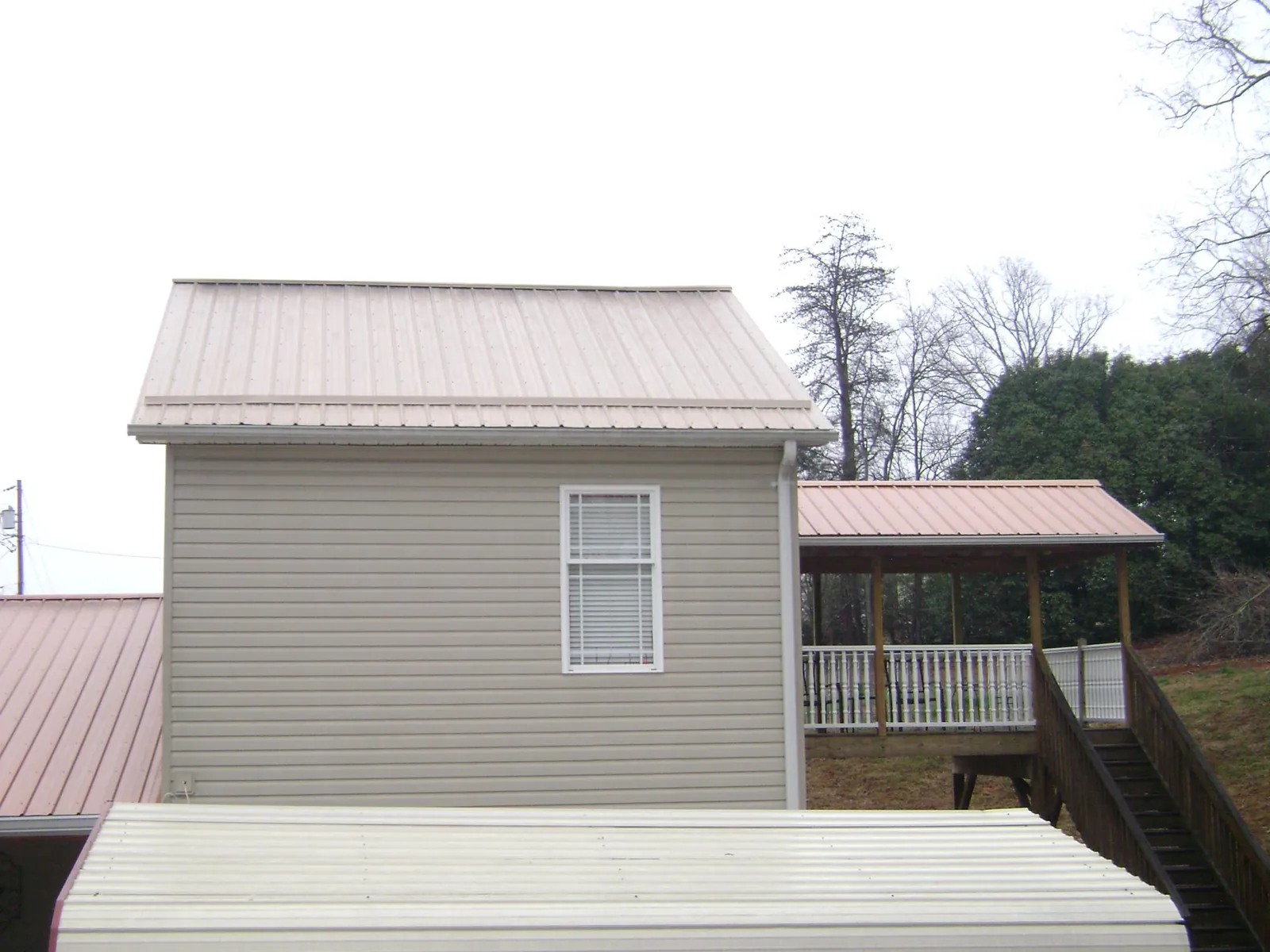 Tan metal roofs on a two story addition and attached porch, from a Roof Replacement job in Port Matilda